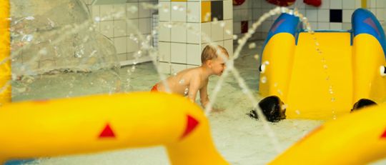 Kind im Kleinkinderbecken mit Wasserspielen und kleiner Rutsche