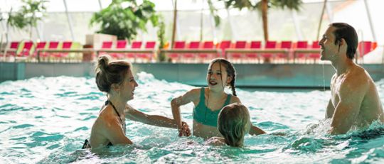Familie tobt gemeinsam in großem Pool mit Wellenbad