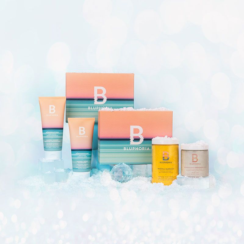 BLUPHORIA Weihnachtsboxen Zwei bunte Verpackungsboxen mit den BLUPHORIA Produkten stehen nebeneinander auf und um weißem Kunstschnee