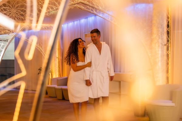 Pärchen in Bademäntel laufen zusammen durch einen warm beleuchteten Gang