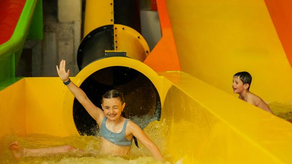 Kind jubelt vor Freude am Ende einer Röhren- Wasserrutsche
