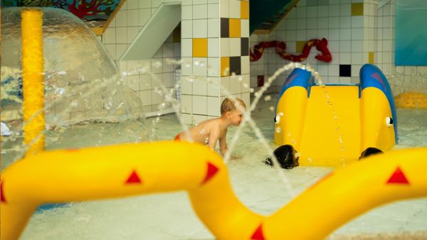 Kind soielt im Kleinkinder-Wasserbecken mit Wasserspielen und kleiner Kleinkinderrutsche