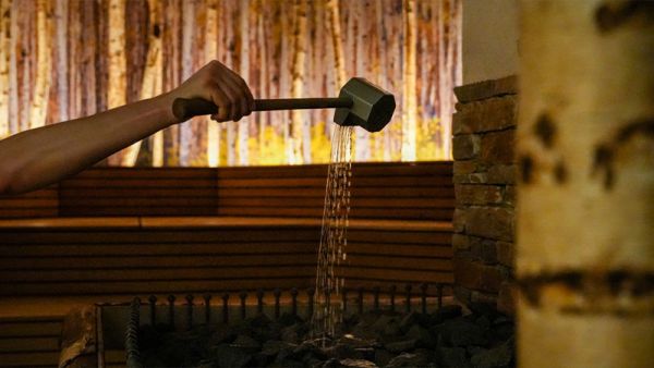 Hand mit Kelle gießt Wasser auf einen Saunaofen