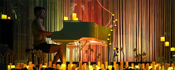 Ein Mann sitzt an einem weißen Flügel umgeben von vielen Kerzen