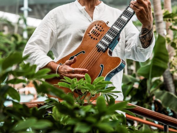 Gitarrenspieler in weißem Tshirt hinter Blättern