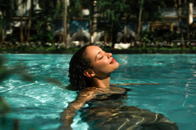 Eine Frau schwimmt mit Blick in den Himmel durch eine Palmenlandschaft 