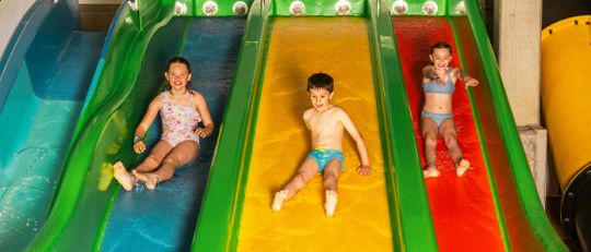 Drei Kinder auf einer Dreier-Wasserrutsche rutschen nebeneinander