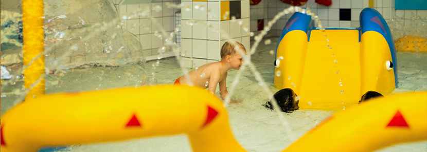 Kind im Kleinkinderbecken mit Wasserspielen und kleiner Rutsche