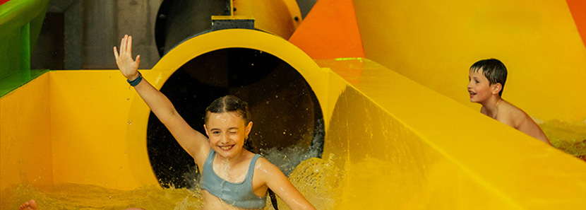 Mädchen kommt aus einer gelb-schwarzen Röhren-Wasserrutsche